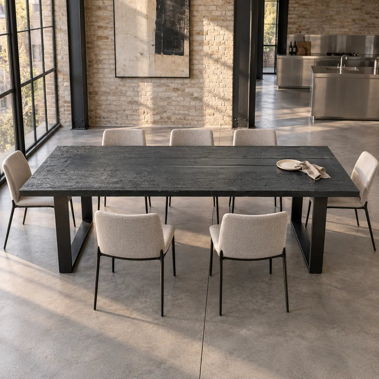 Table Zenith noire vue de face, avec chaises claires devant un mur de briques et de grandes fenêtres.