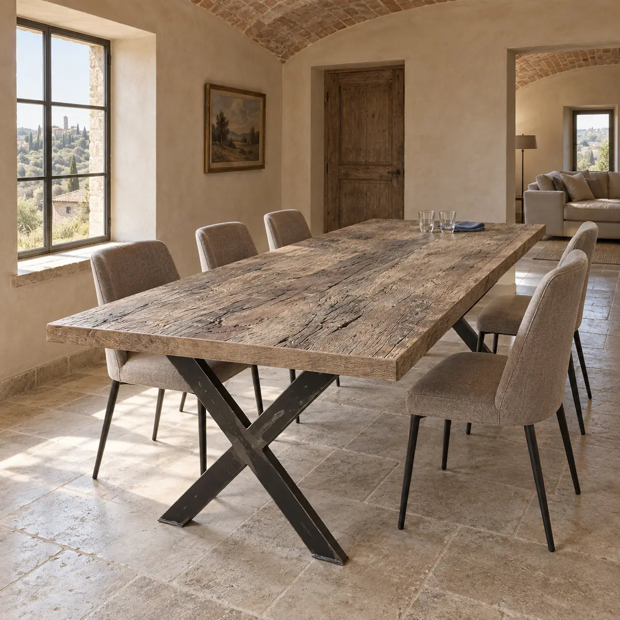 Table Toscane avec piètements en X et chaises claires, sous un plafond voûté en briques.